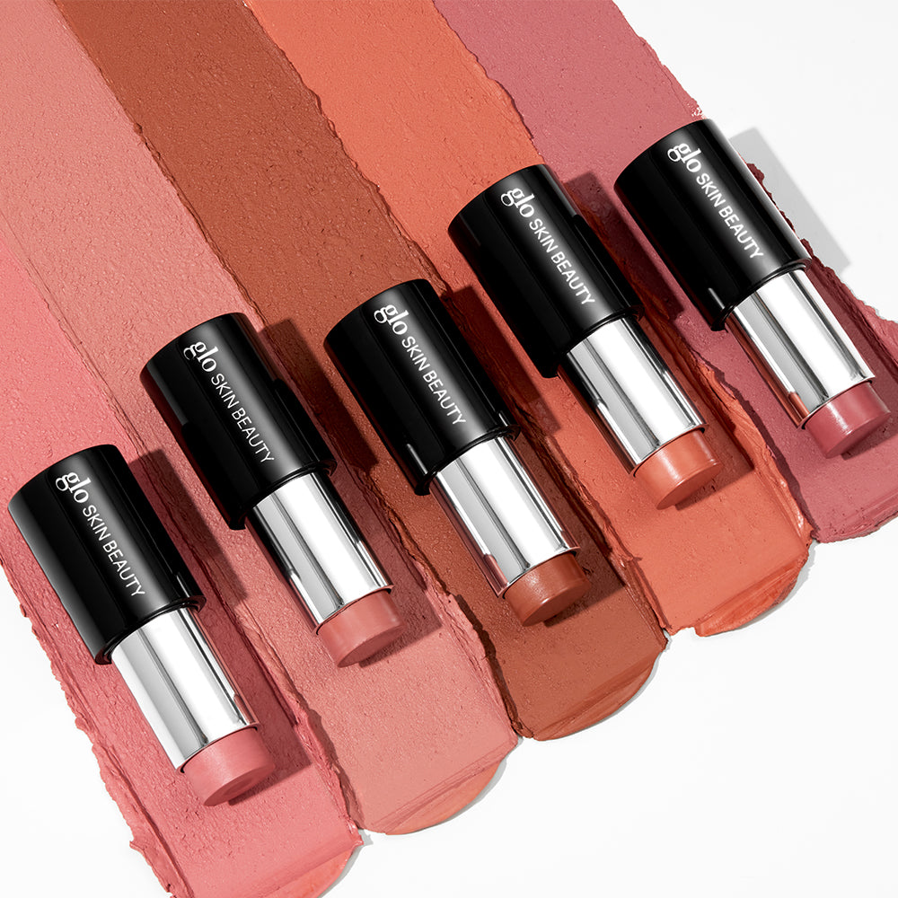 Five rosy-nude lipstick sticks labeled glo SKIN BEAUTY laid over matching smeared color swatches