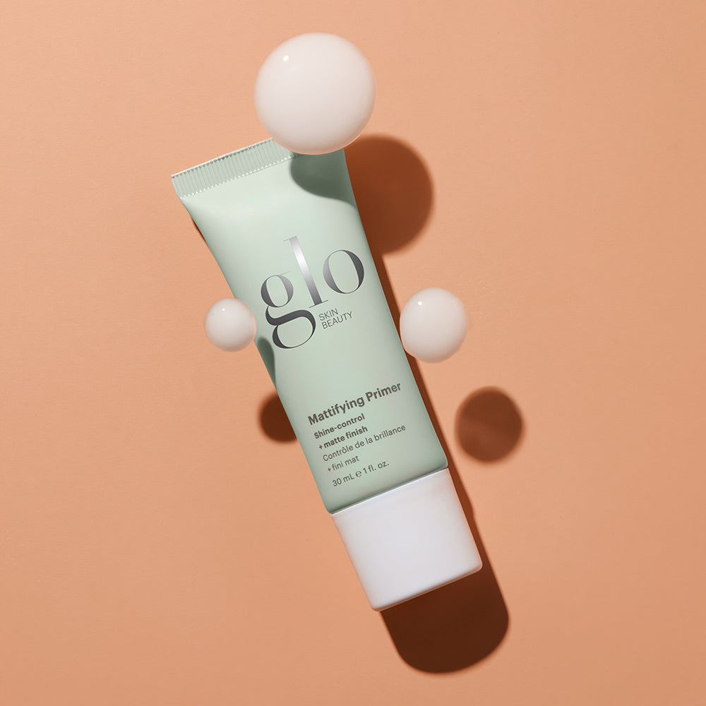 glo SKIN BEAUTY Mattifying Primer tube on peach background with three cream droplets and shadow.