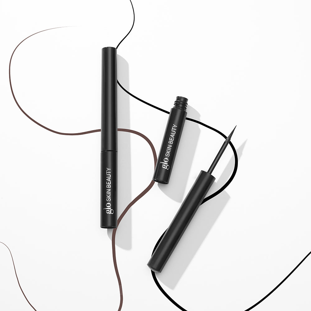 Two black glo SKIN BEAUTY liquid eyeliner tubes with brown and black drawn eyeliner strokes