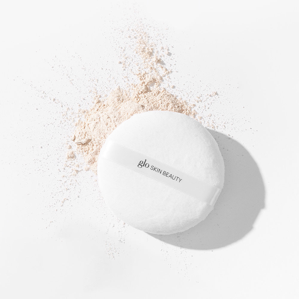 Round makeup powder puff with loose translucent powder and ribbon labeled glo SKIN BEAUTY.