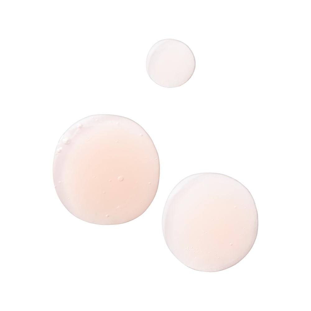 Three light pink serum drops of varying sizes on a white background