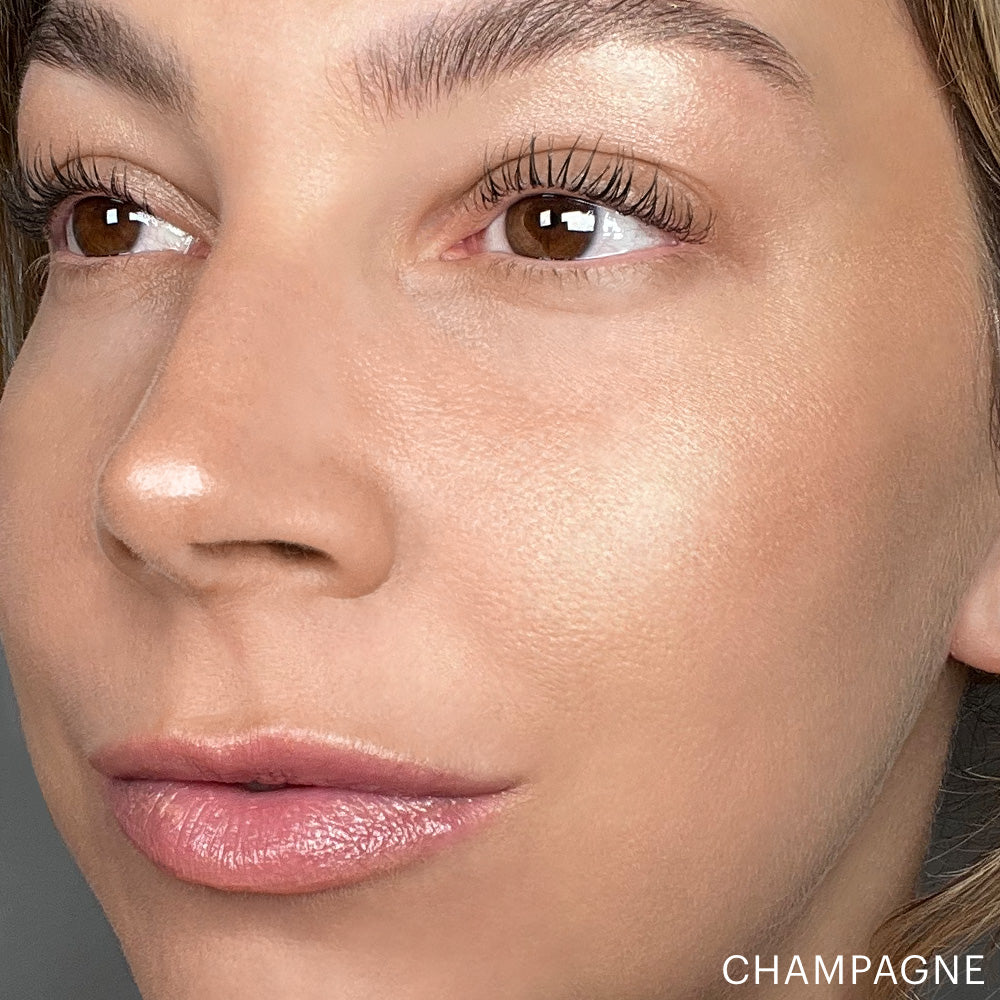 Close-up of a woman's face showing skin glow powder highlighter on cheek labeled 'CHAMPAGNE'