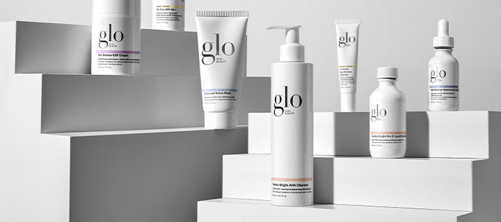 Assortment of white glo skincare bottles and tubes arranged on stepped white display platforms