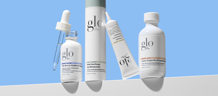 Four glo Skin Beauty skincare products — dropper bottle, tall moisturizer, tube, and liquid bottle on pale blue background