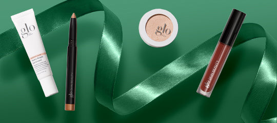 'glo' cosmetics: tube, eyebrow pencil, compact labeled 'glo', and brown lip gloss on green satin ribbon.