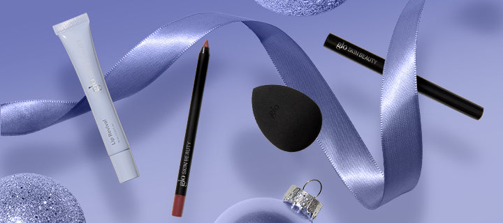 Lavender flat-lay of beauty items: tube, brown lip liner, black blending sponge, two black eye pencils and silver ornament.