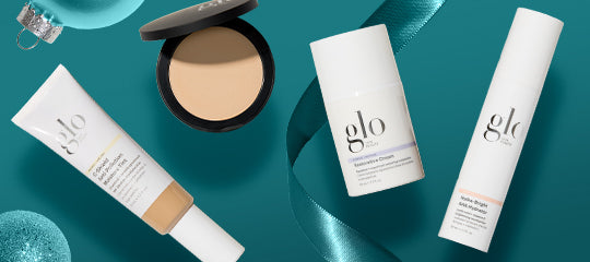 Assortment of glo skincare and makeup products — compact, cream tube, and pump bottles on teal background with ribbon.